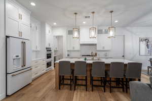 Kitchen with decorative light fixtures, white appliances, light wood-type flooring, a breakfast bar area, and white cabinets