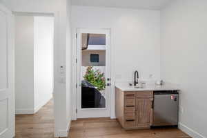 Bar area featuring light wood-style flooring, stainless steel fridge, light stone counters, and wood finish cabinets