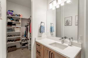 Bathroom with vanity, light colored carpet, and a walk in closet