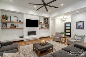 Living room with a fireplace, recessed lighting, ceiling fan with notable chandelier, and light wood finished floors