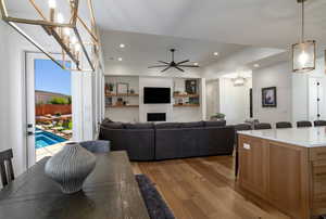 Living room featuring ceiling fan, light wood finished floors, suspended lighting, a brick fireplace, and built in shelves