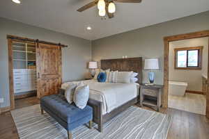 Bedroom with a barn door, a walk in closet, wood-type flooring, baseboards, and recessed lighting