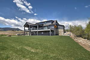 Back of property featuring a deck with mountain view, a lawn, and stone siding