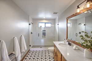 Full bath featuring toilet, vanity, a shower stall, baseboards, and visible vents