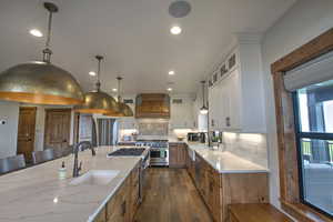 Kitchen with light stone countertops, stainless steel appliances, a sink, custom range hood, and dark wood-style floors