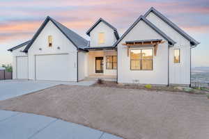 Modern farmhouse featuring a porch, an attached garage, concrete driveway, board and batten siding, and fence