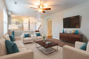 Living room with ceiling fan, light carpet, arched walkways, stairs, and visible vents