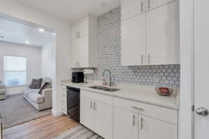 Kitchen featuring open floor plan, light countertops, a sink, light wood-style floors, and black dishwasher