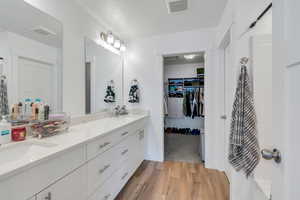 Full bath with double vanity, visible vents, wood finished floors, and a sink