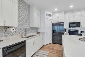 Kitchen featuring white cabinetry, a sink, light wood-style floors, and black appliances