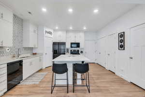 Kitchen featuring light countertops, a breakfast bar, a sink, black appliances, and backsplash