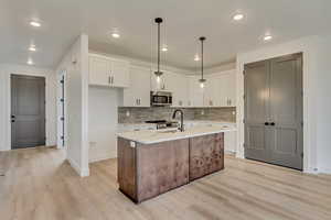 Kitchen featuring white cabinets, tasteful backsplash, stainless steel appliances, and light wood finished floors