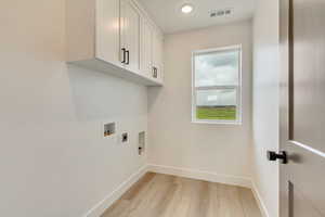 Washroom featuring light wood-type flooring, baseboards, visible vents, cabinet space, and electric dryer hookup