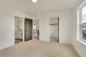 Unfurnished bedroom featuring light carpet, ensuite bath, and baseboards