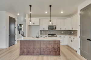 Kitchen featuring white cabinets, stainless steel appliances, decorative backsplash, and light wood-style floors