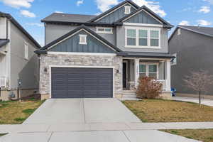 Craftsman inspired home featuring stone siding, board and batten siding, concrete driveway, and roof with shingles