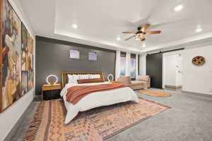 Master bedroom featuring carpet floors, a tray ceiling, a barn door, and recessed lighting