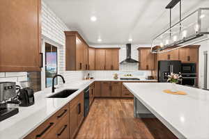 Kitchen featuring light countertops, backsplash, a sink, wall chimney exhaust hood, and black appliances