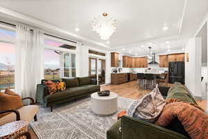 Living room with a tray ceiling, an inviting chandelier, recessed lighting, and light wood finished floors