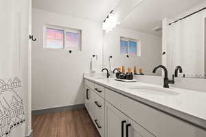 Full bath with baseboards, wood finished floors, double vanity, and a sink