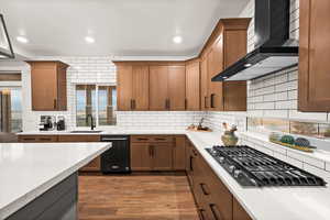 Kitchen featuring stainless steel gas cooktop, wall chimney exhaust hood, light countertops, and a sink