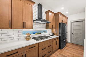 Kitchen featuring stainless steel gas stovetop, light countertops, high end black fridge, wall chimney exhaust hood, and light wood-style floors