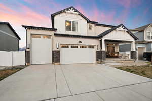 View of front of house featuring concrete driveway, stucco siding, fence, stone siding, and board and batten siding