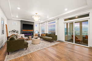 Living room with a large fireplace, a tray ceiling, wood finished floors, and an inviting chandelier