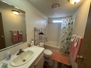Bathroom with wallpapered walls, shower / bath combo with shower curtain, toilet, and wood finished floors