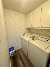 Clothes washing area featuring washer and clothes dryer, a textured ceiling, wallpapered walls, cabinet space, and dark wood-type flooring