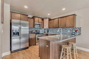 Kitchen featuring a sink, appliances with stainless steel finishes, a peninsula, light wood-style flooring, and decorative backsplash
