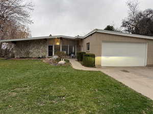 Mid-century modern home with stone and brick siding, a garage, a front lawn, and concrete driveway