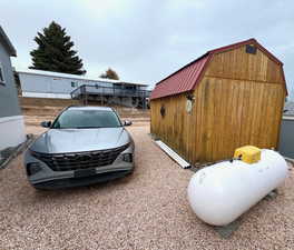 Back of home with parking area, propane tank and shed