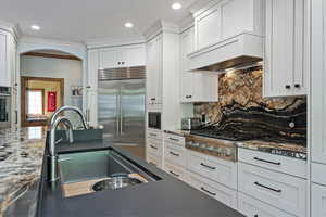 Kitchen with stainless steel appliances, premium range hood, white cabinets, and arched walkways