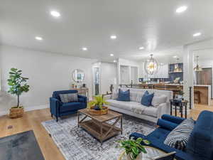 Living area with baseboards, light wood-type flooring, recessed lighting, and an inviting chandelier