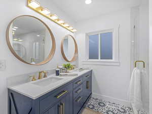 Full bath with double vanity, a sink, a shower with shower door, and baseboards
