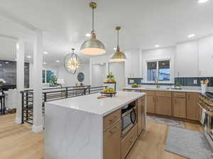 Kitchen featuring decorative backsplash, stainless steel microwave, decorative light fixtures, light wood-style floors, and a center island