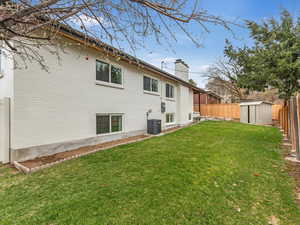 Exterior space featuring central AC unit, a chimney, a fenced backyard, a lawn, and an outdoor structure