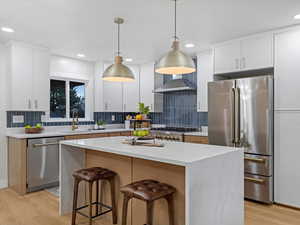 Kitchen with white cabinetry, a center island, appliances with stainless steel finishes, and light wood-style floors