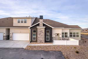 View of front of house with stone siding, driveway, fence, a garage, and stucco siding