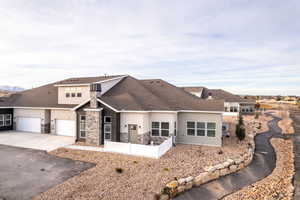 View of front of home with a shingled roof, driveway, stucco siding, and stone siding
