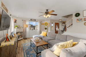 Living area featuring stairs, light wood-style floors, and a ceiling fan