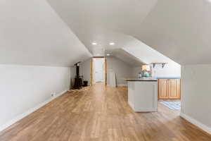 Bonus room featuring lofted ceiling, a wood stove, baseboards, light wood-style floors, and visible vents