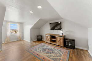 Additional living space with baseboards, vaulted ceiling, wood finished floors, and a textured ceiling
