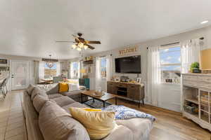 Living room with a wainscoted wall, wood finished floors, and ceiling fan with notable chandelier