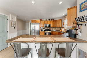 Kitchen featuring a kitchen bar, light tile patterned flooring, a peninsula, appliances with stainless steel finishes, and wainscoting