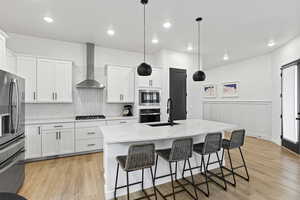 Kitchen with wall chimney range hood, a sink, appliances with stainless steel finishes, and light wood-style floors