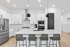 Kitchen featuring stainless steel fridge with ice dispenser, white cabinets, wall chimney exhaust hood, and built in microwave
