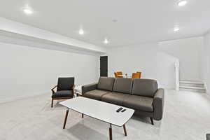 Living room with stairway, baseboards, light colored carpet, and recessed lighting