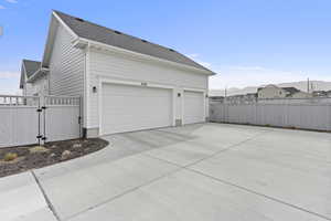 View of side of home with driveway, a gate, fence, and roof with shingles